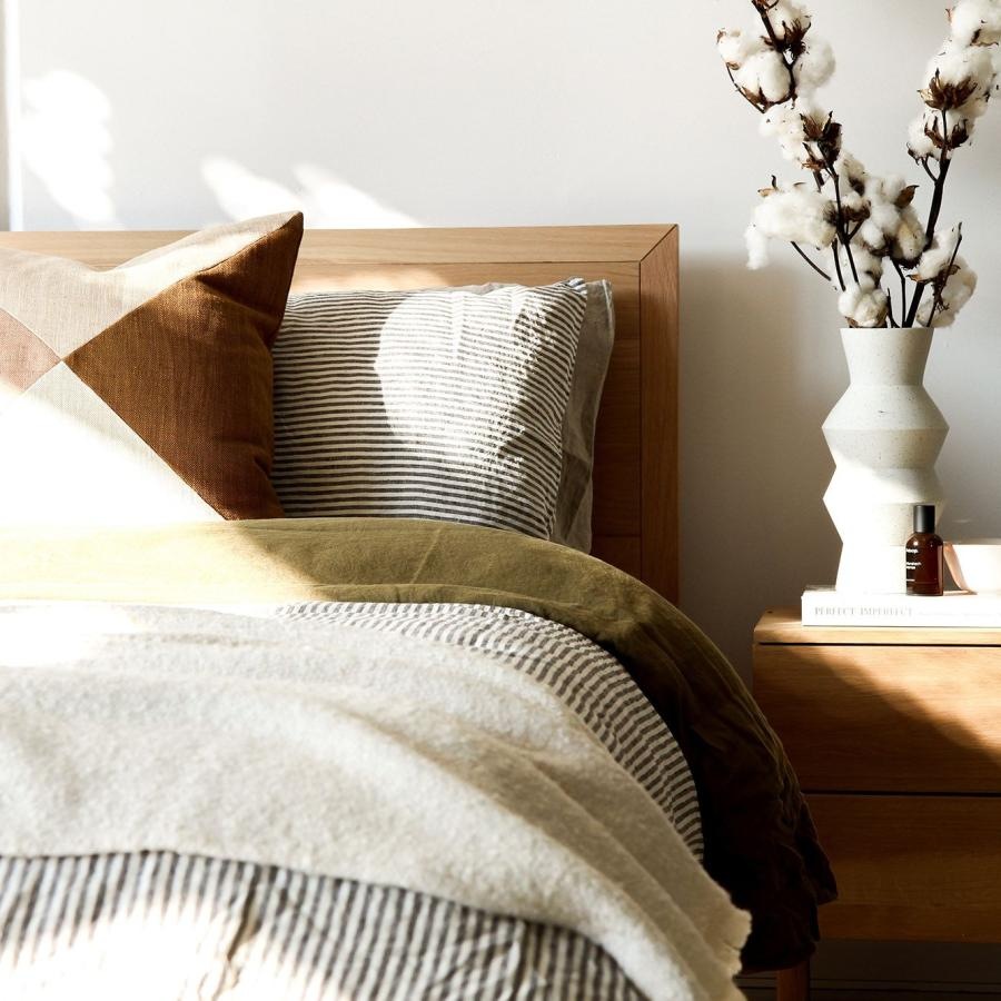 Sleep in style swath of sunlight shines across a well made bed and bedside table with a vase of cotton plants